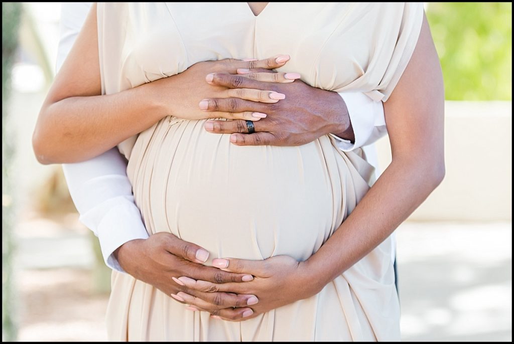 picture of a pregnant African American women in a tan maternity gown and her husbands hand on her belly at Scottsdale Civic Center